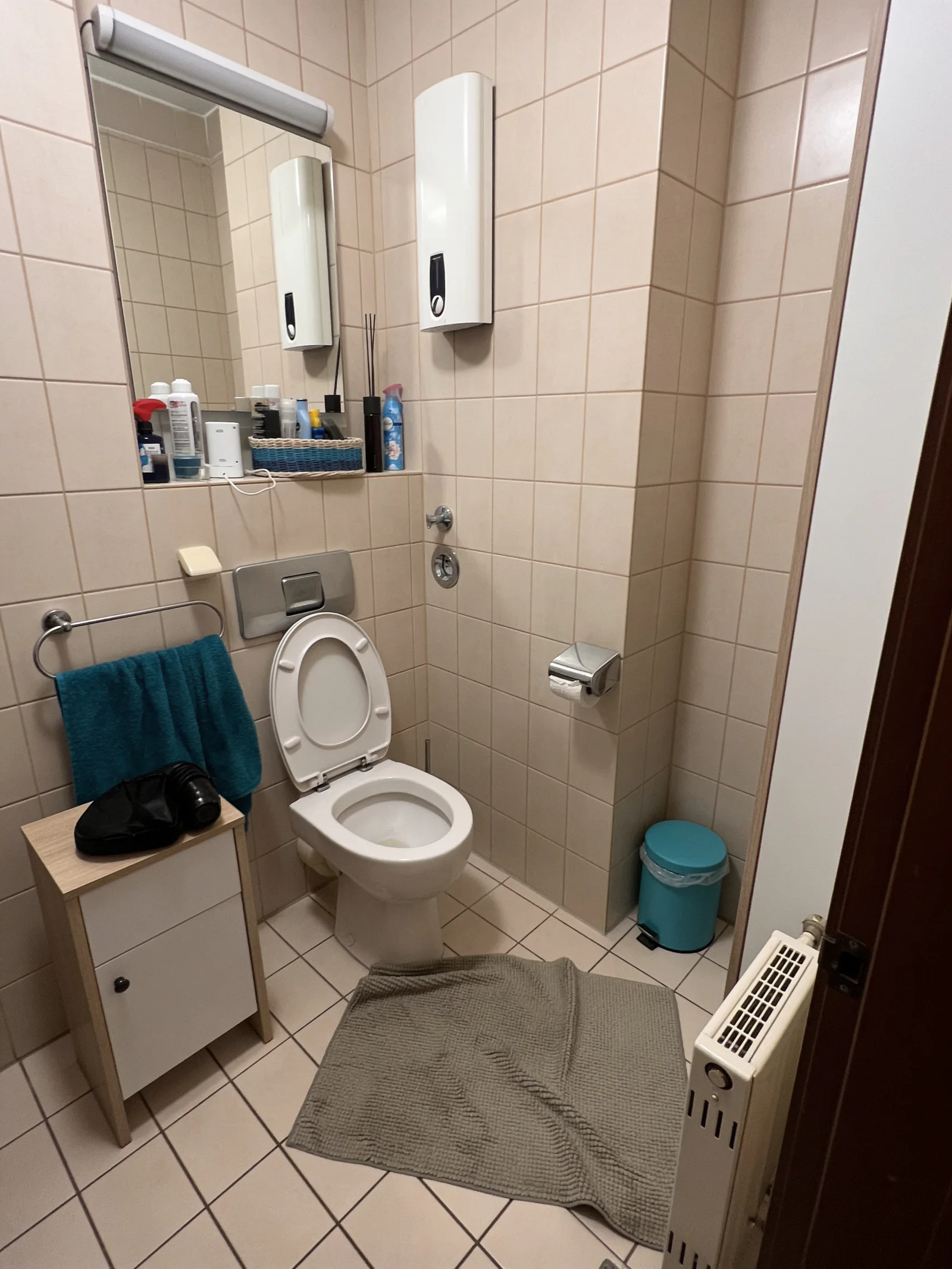 Kleines, beige gefliestes Bad vor der Sanierung mit Stand-WC, Spiegel und schmalem Unterschrank