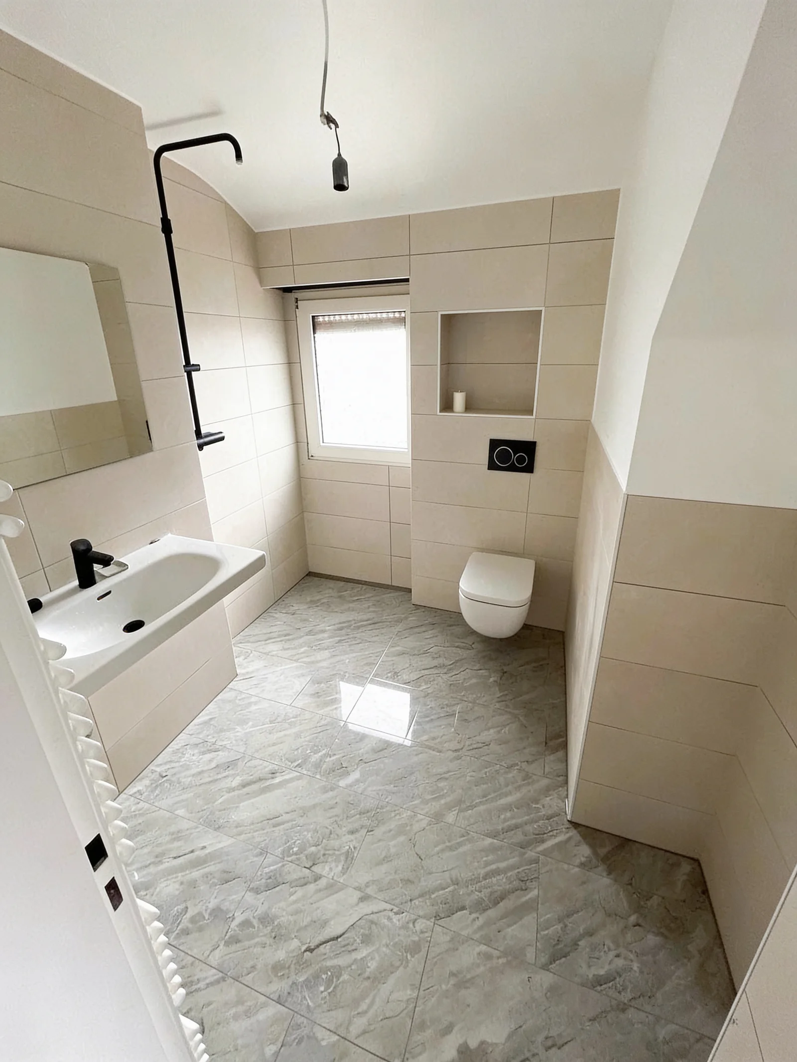 Modernisiertes Bad mit beigefarbenen Wandfliesen, grauem Boden, bodengleicher Dusche, Wandnische und wandhängendem WC